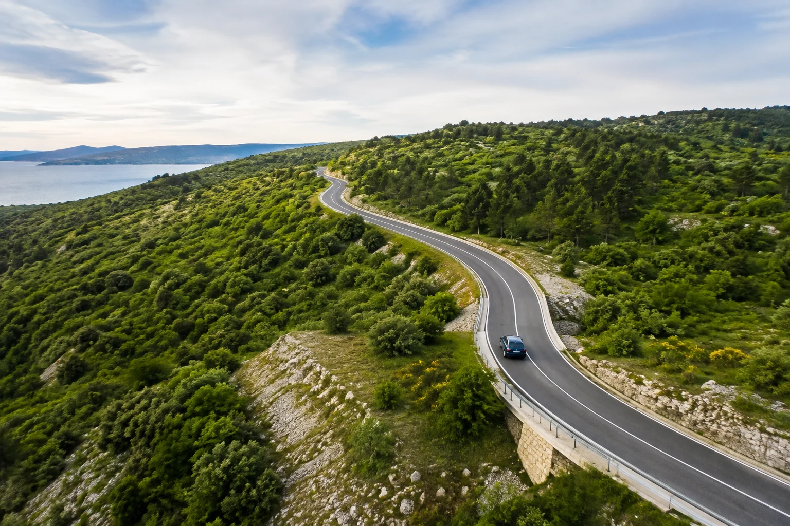 A winding road through a green landscape with a car in the distance